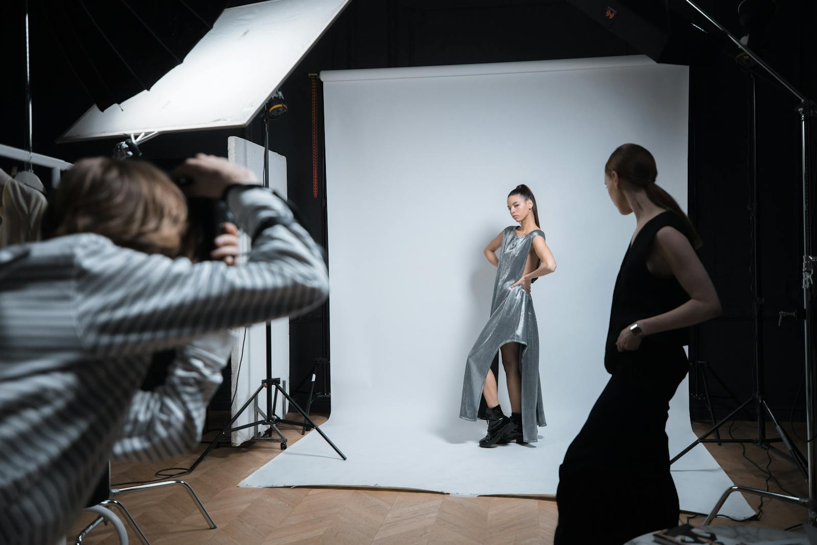 A working set in the Mira Beauty Lagos studio — two stylists pinning a garment on a model while a photographer reviews tethered captures on a calibrated monitor.